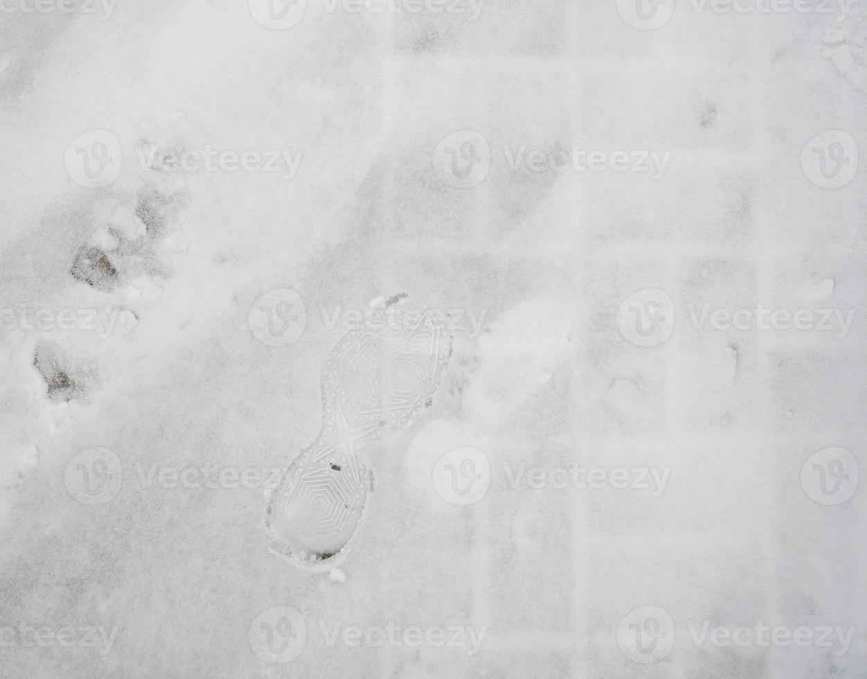 Footprint in the snow from a boot. Snowy street tiles texture. photo