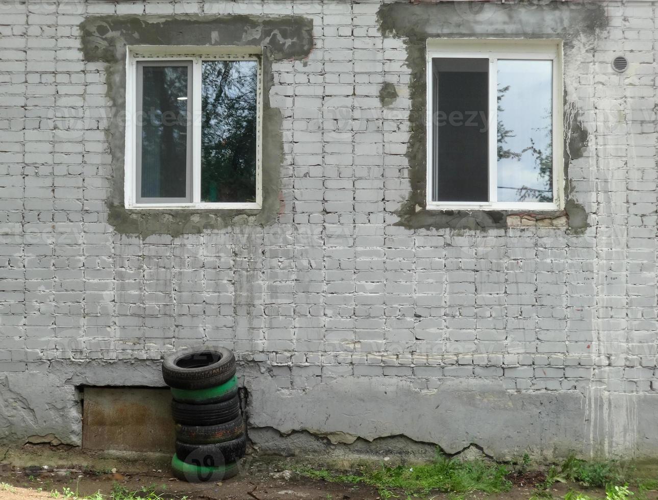 Nuevas ventanas en la barriada. casa antigua. choza. neumáticos de coche apilados foto