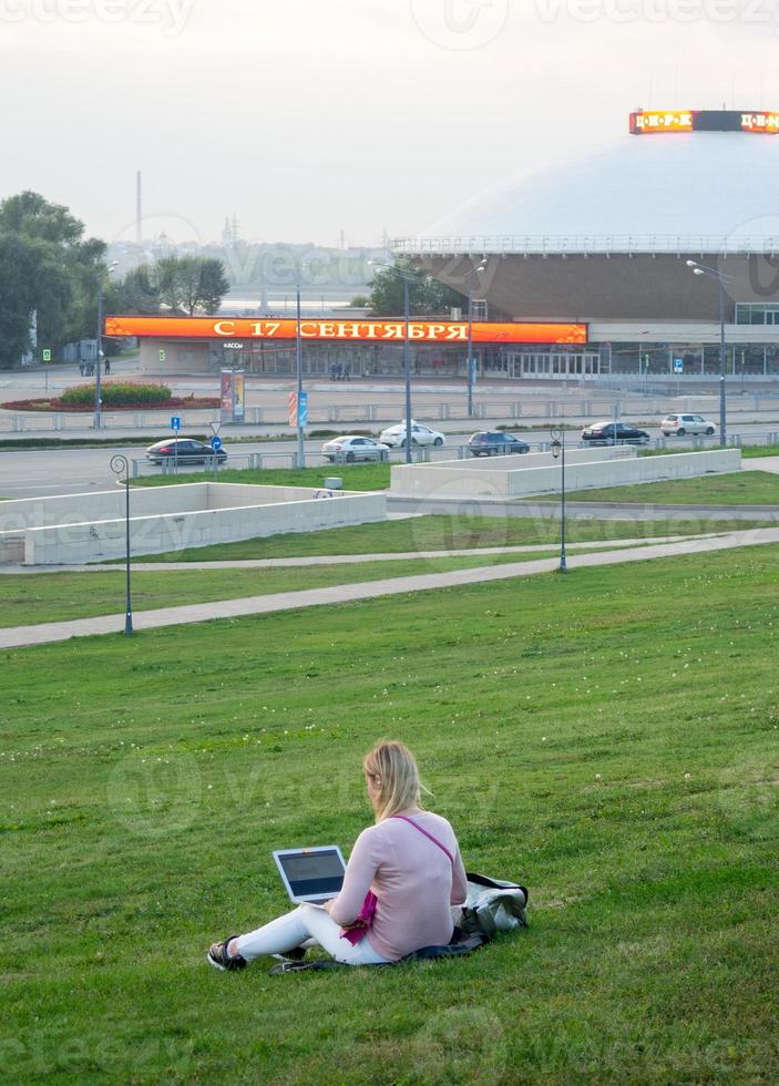 Girl working in a laptop on the lawn in the city photo