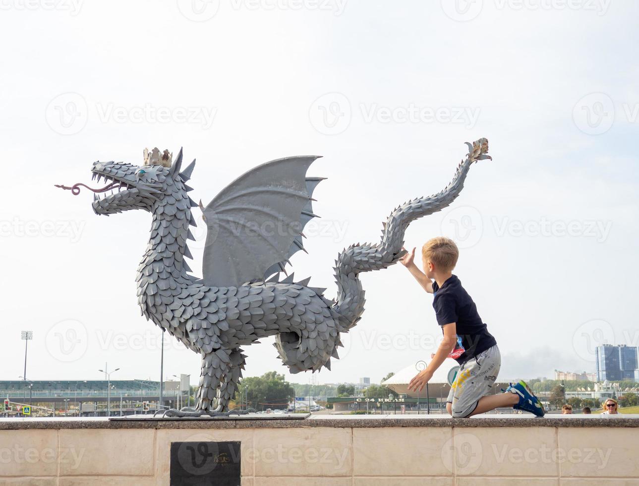The boy touches the dragon statue. The symbol of the city. photo
