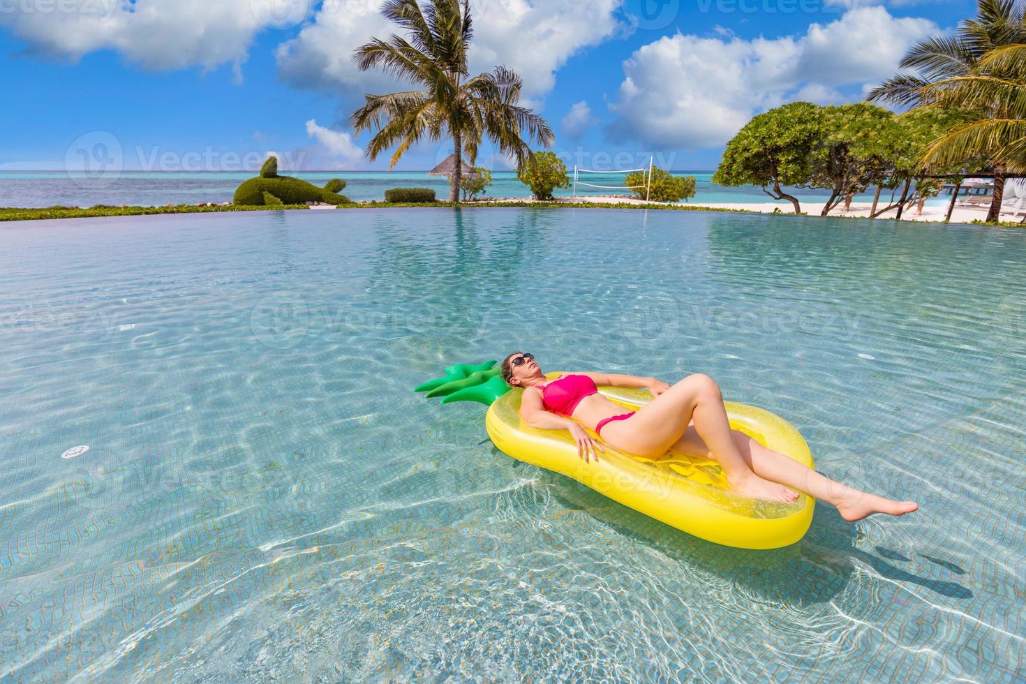 hermosa mujer sexy relajándose en el complejo tropical de la piscina inflable de goma. atractiva mujer delgada despreocupada disfrutando del clima caluroso de verano en bikini rosa. concepto de estilo de vida de ocio de libertad de vacaciones foto