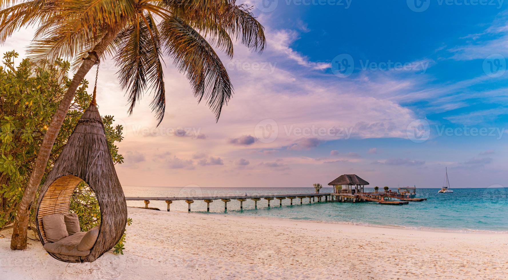 panorama tropical de la playa de puesta de sol como paisaje de verano con columpio de playa relajante o hamaca en palmeras de coco, arena blanca y pancarta de playa de mar tranquilo. perfectas vacaciones en la playa o concepto panorámico de vacaciones de verano foto