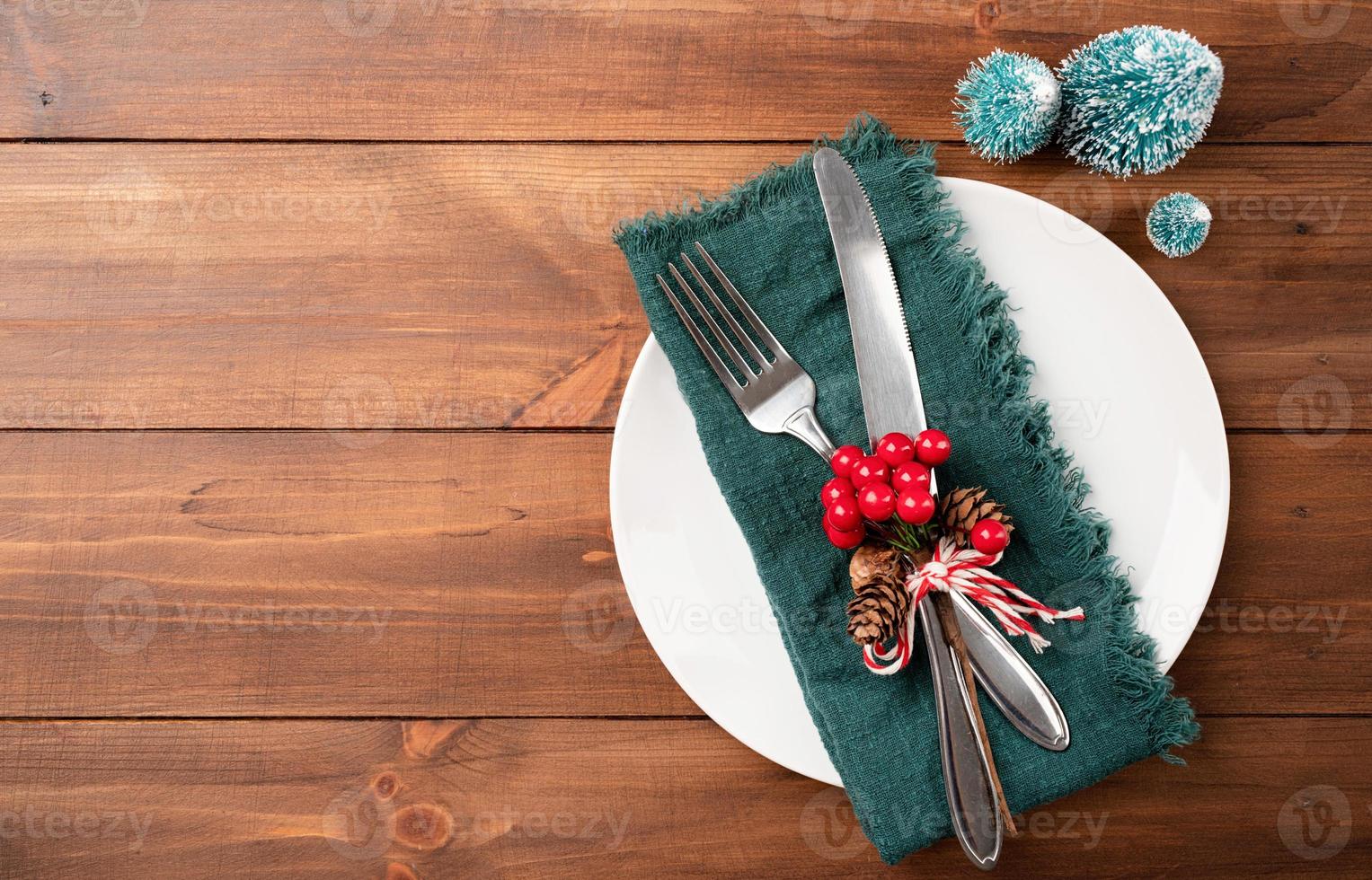Christmas table setting with white dishware, silverware and green decorations on wooden background. Top view. photo