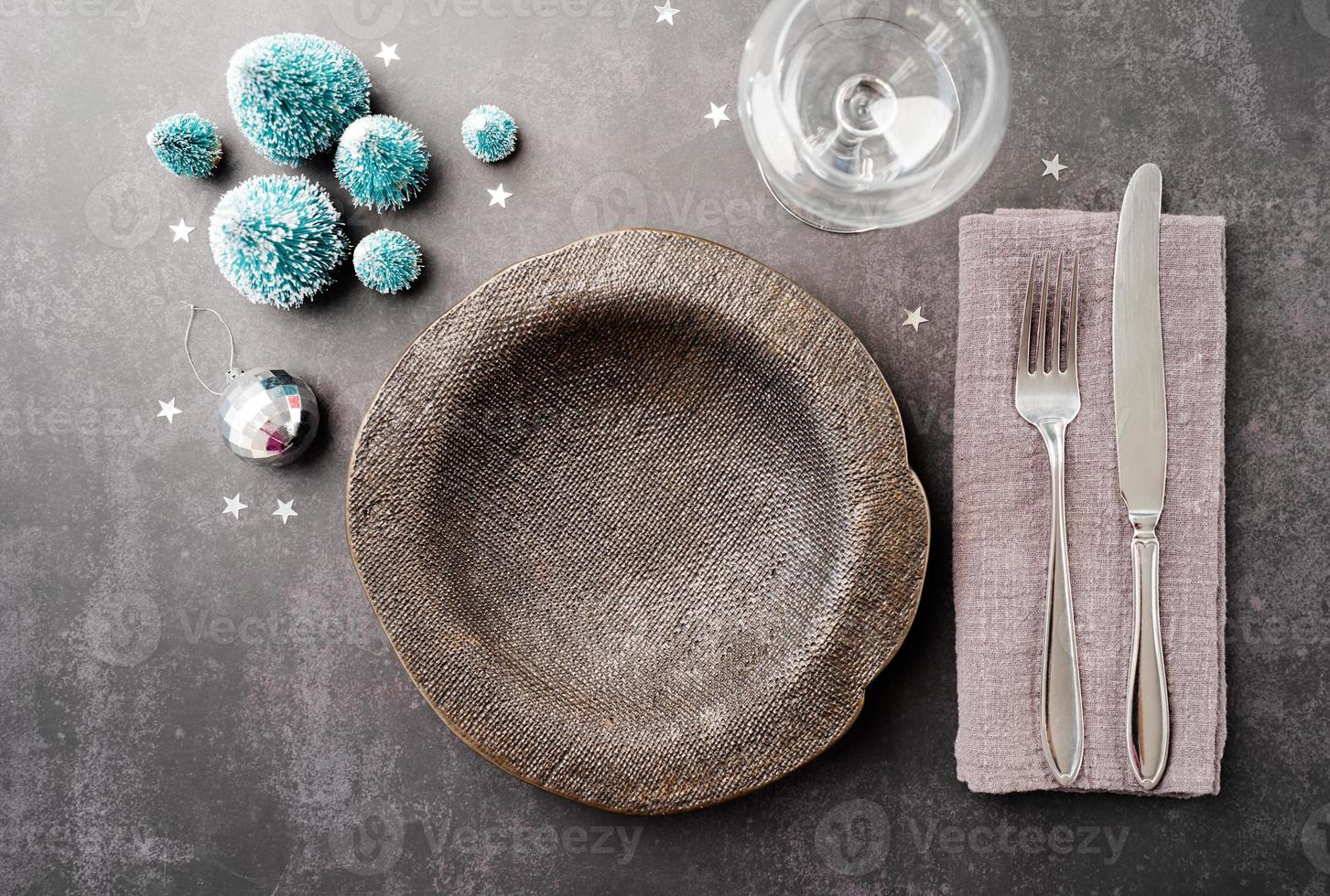 Christmas table setting with black dishware, silverware and green decorations on dark background. Top view. photo