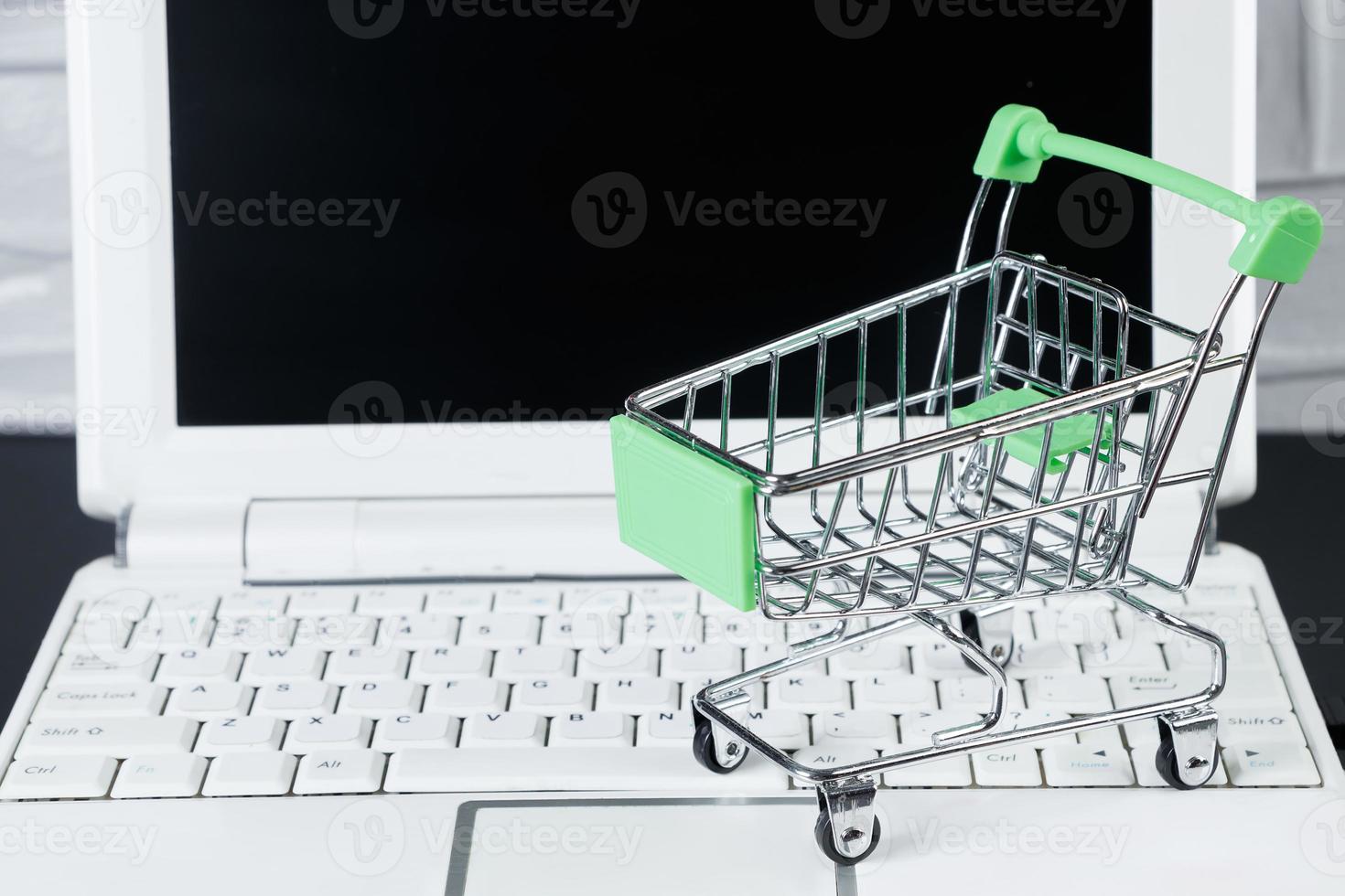 Online sale and Black Friday concept. Laptop and mini shopping cart on white background. photo