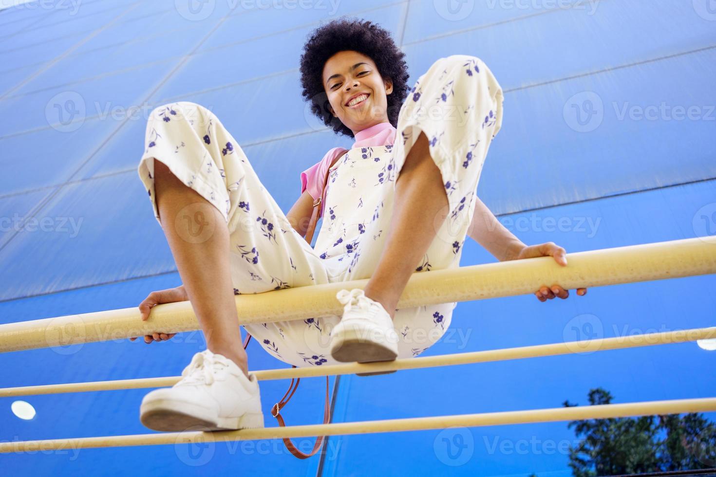 Smiling black woman sitting on fence in city photo