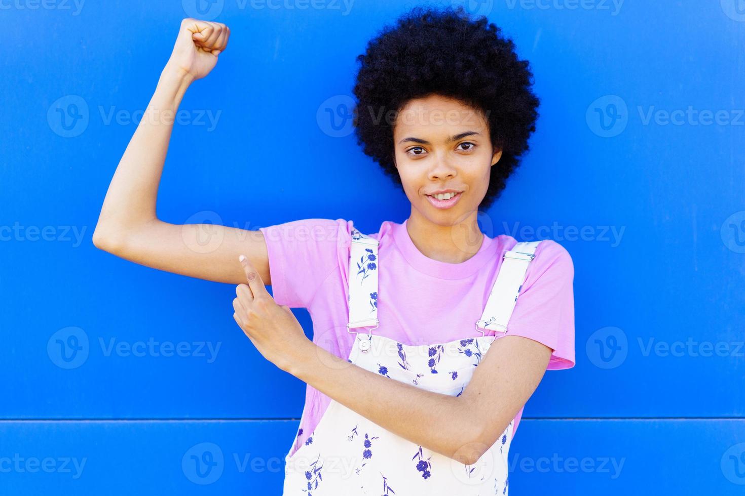 mujer negra mostrando músculos cerca de la pared azul foto