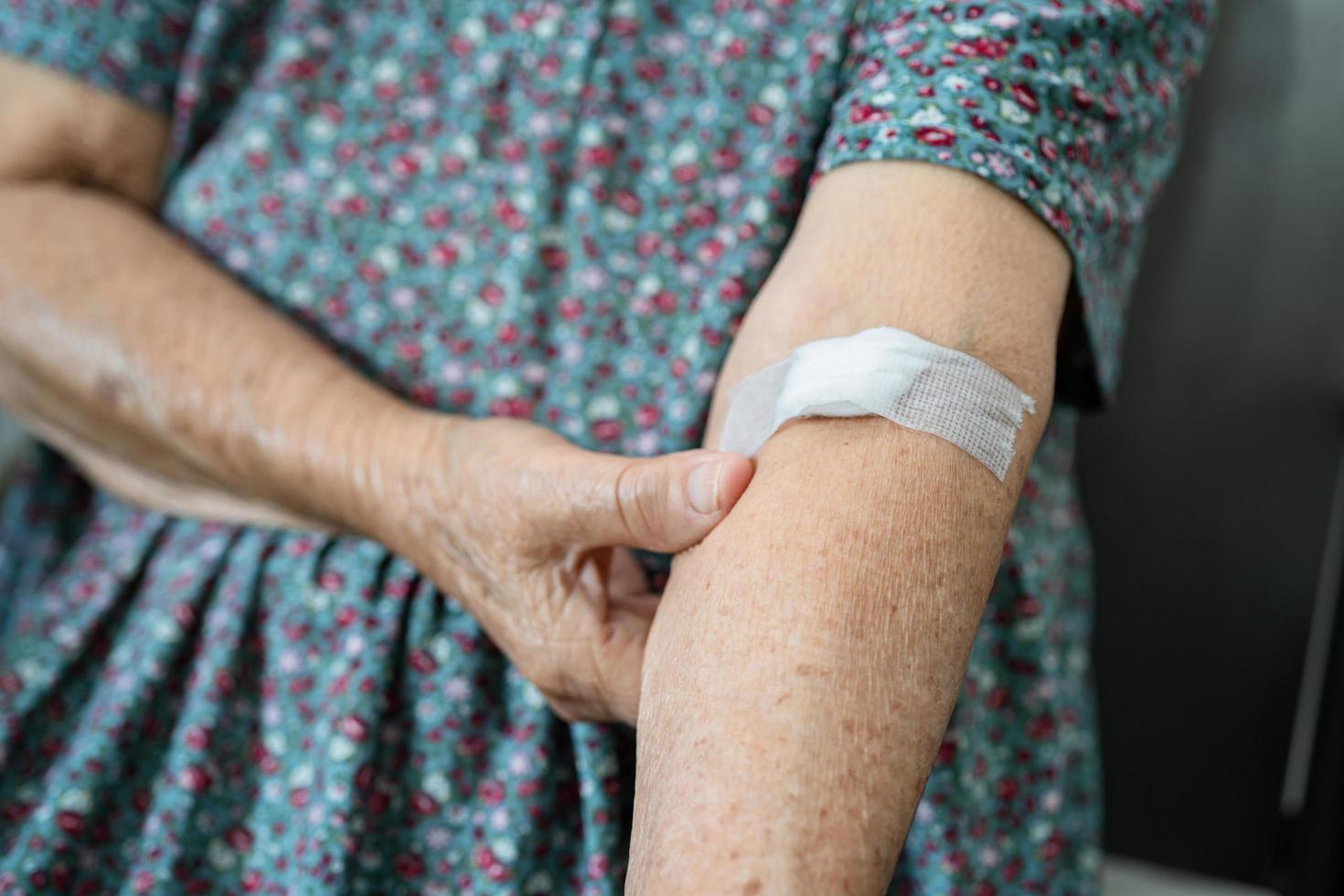 Asian senior or elderly old lady woman patient show cotton wool stop bleeding, after blood drawing testing for annually physical health check up to check cholesterol, blood pressure, and sugar level. photo