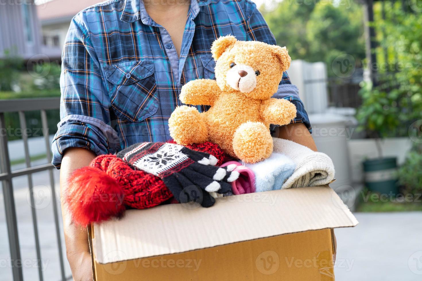 Holding clothing donation box with used clothes and doll at home to support help for poor people in the world. photo
