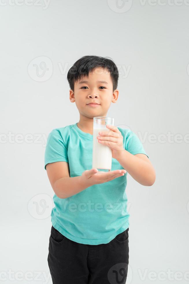 Cute boy in blue shirt holding glass of milk on white background photo