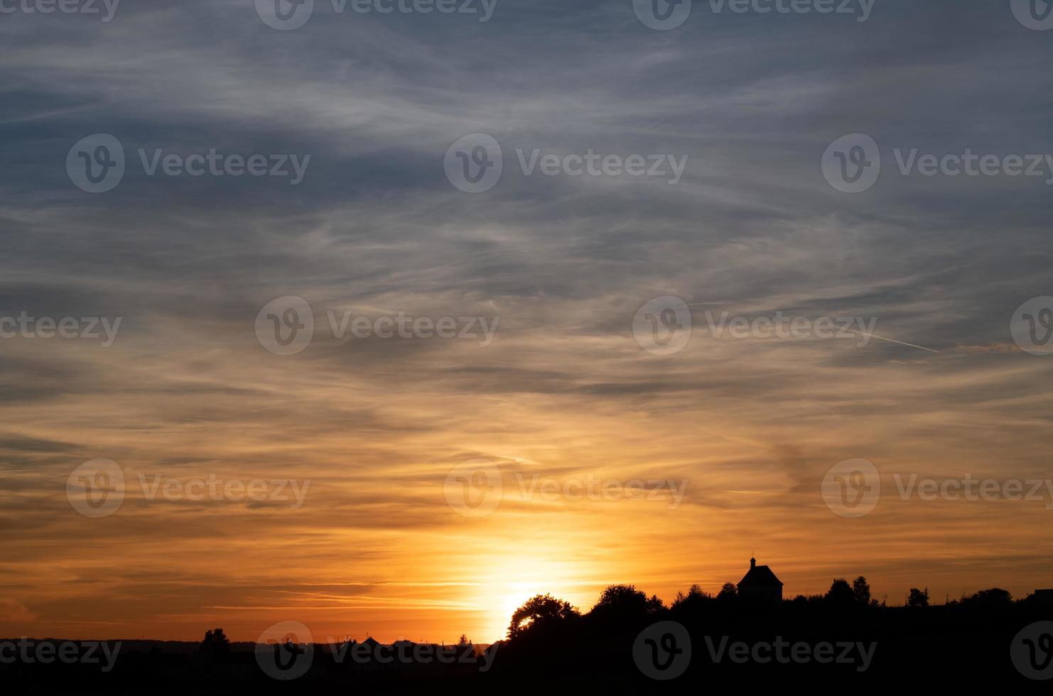 espectacular puesta de sol en baviera. el cielo está lleno de nubes. los colores cambian de rojo a azul. al fondo la sombra de un pequeño pueblo. una capilla se encuentra en una pequeña colina. foto