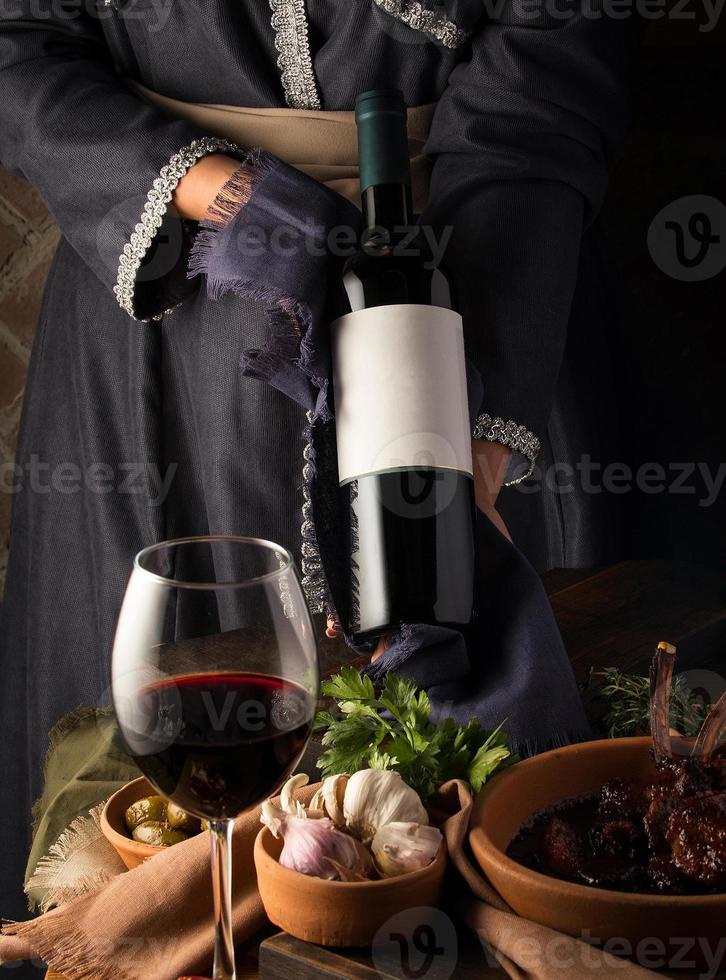 A vertical shot of a person in a traditional costume showing a wine bottle photo