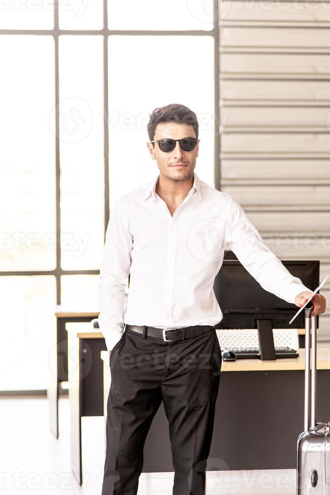 Young and smart businessman with sunglasses, suitcase and travel document such as air ticket, hotel booking document and passport with travel concept,summer vacation concept, summer holiday concept photo
