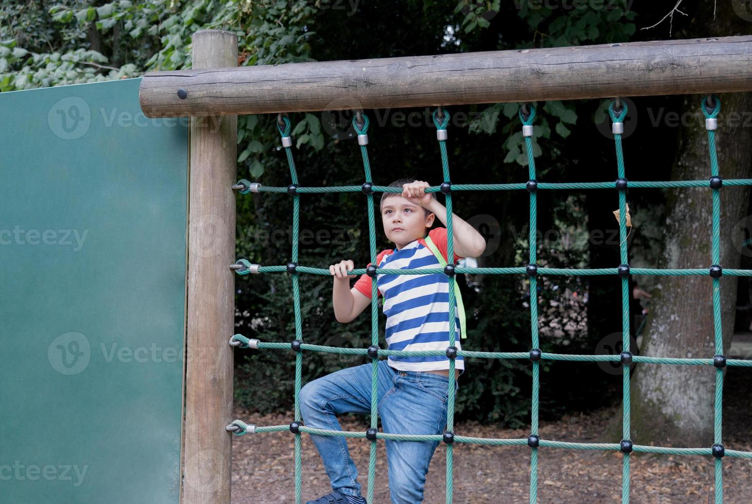 Portrait Kid holding robe in outdoors playground, Child climbing adventure park on sunny day  Spring or sSmmer, Lonely young boy playing alone in public playground. photo