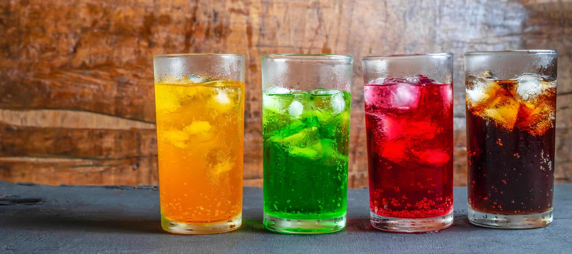 un montón de refrescos en vasos coloridos y sabrosos sobre la mesa,vasos con bebidas dulces con cubitos de hielov foto