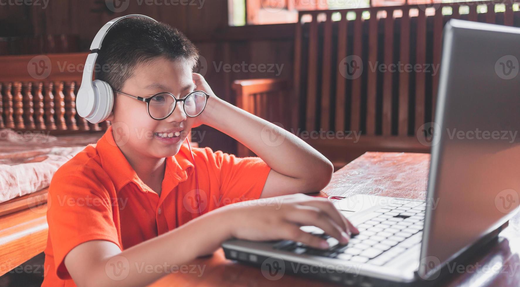 Asian child boy in headphones is using a laptop and studying online with a video call teacher at home. homeschooling, distant learning photo