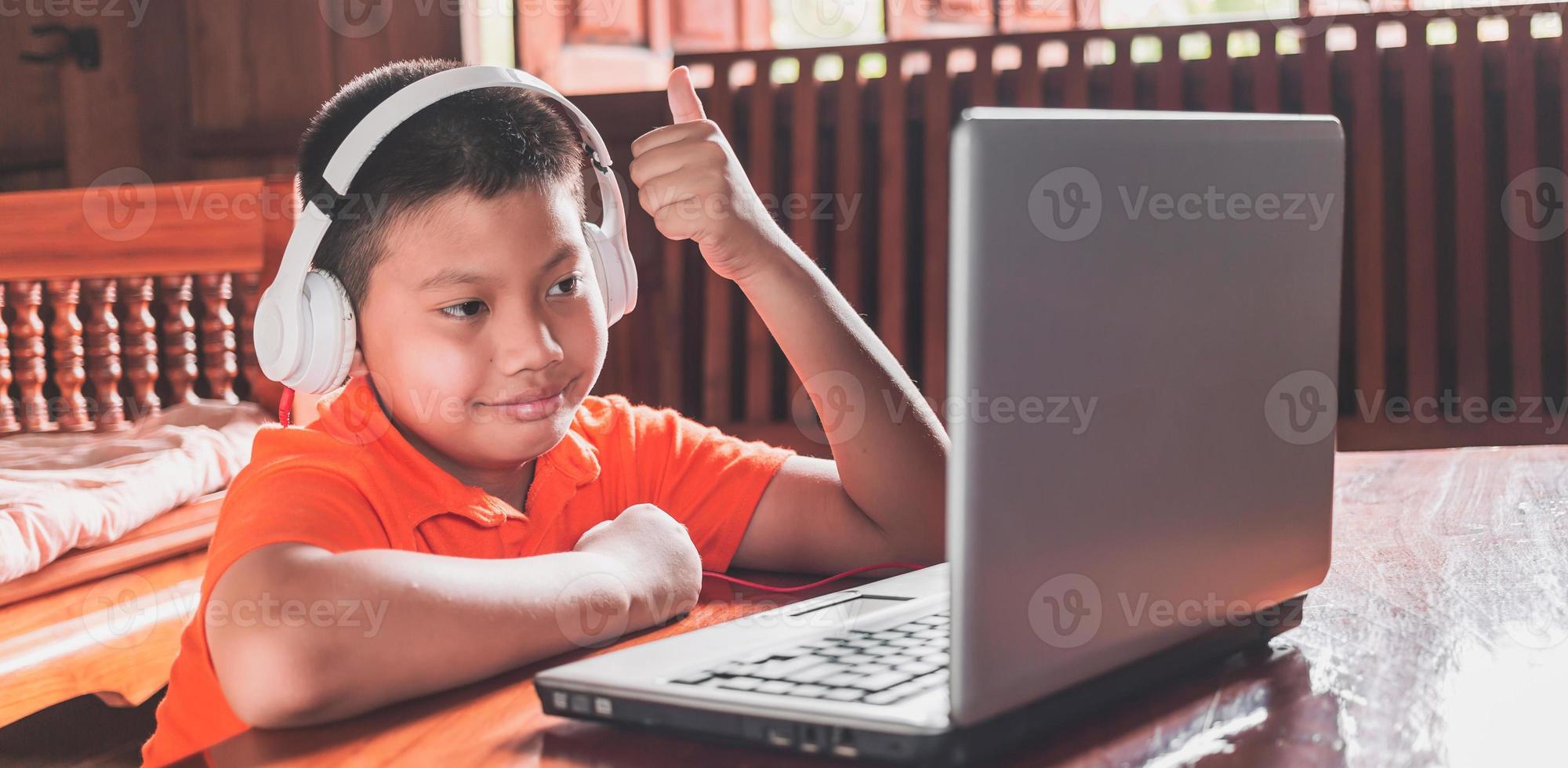 Asian child boy in headphones is using a laptop and studying online with a video call teacher at home. homeschooling, distant learning photo