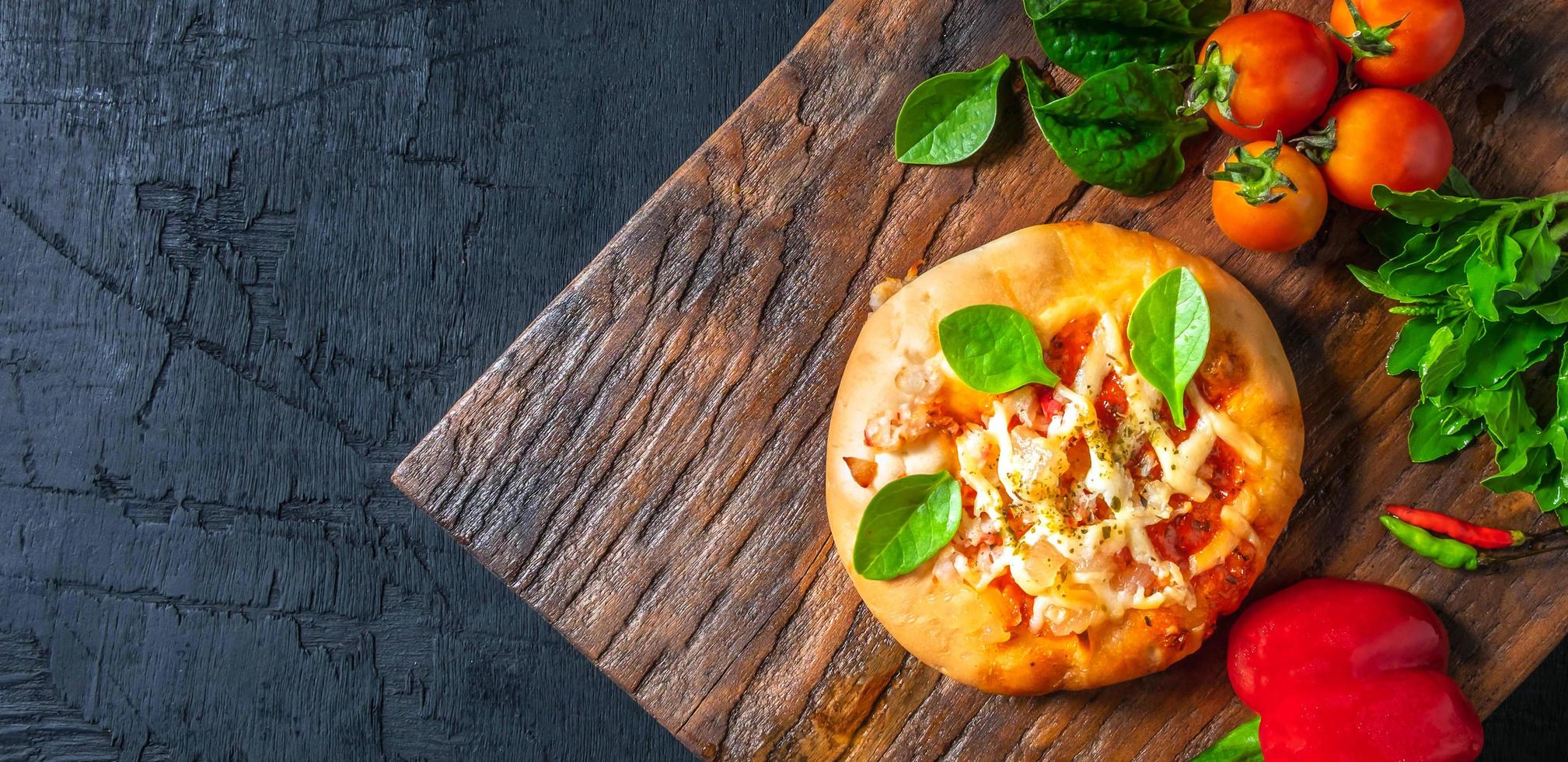 Top view of home made pizza, vegetables, ingredients on a Black wooden  background. Pizza is cooking in the wooden chopping board . Pizza menu. photo