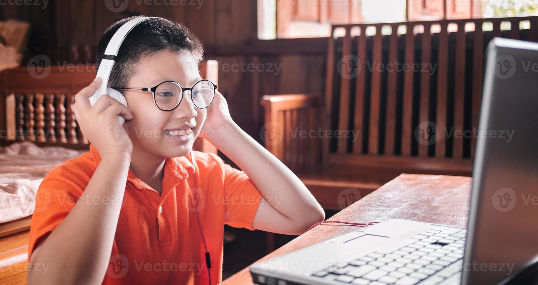 Asian child boy in headphones is using a laptop and studying online with a video call teacher at home. homeschooling, distant learning photo