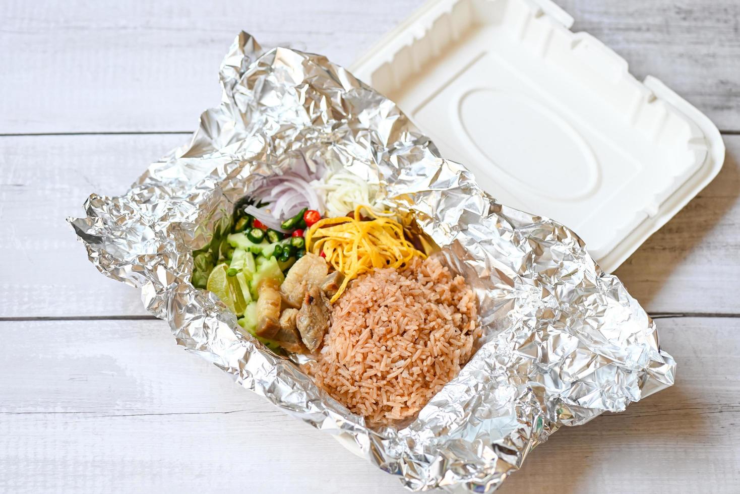 comida tailandesa en caja con envoltura de papel de aluminio comida para llevar - arroz mezclado con pasta de camarones arroz frito en caja, arroz sazonado con receta de pasta de camarones, especias de hierbas de arroz foto