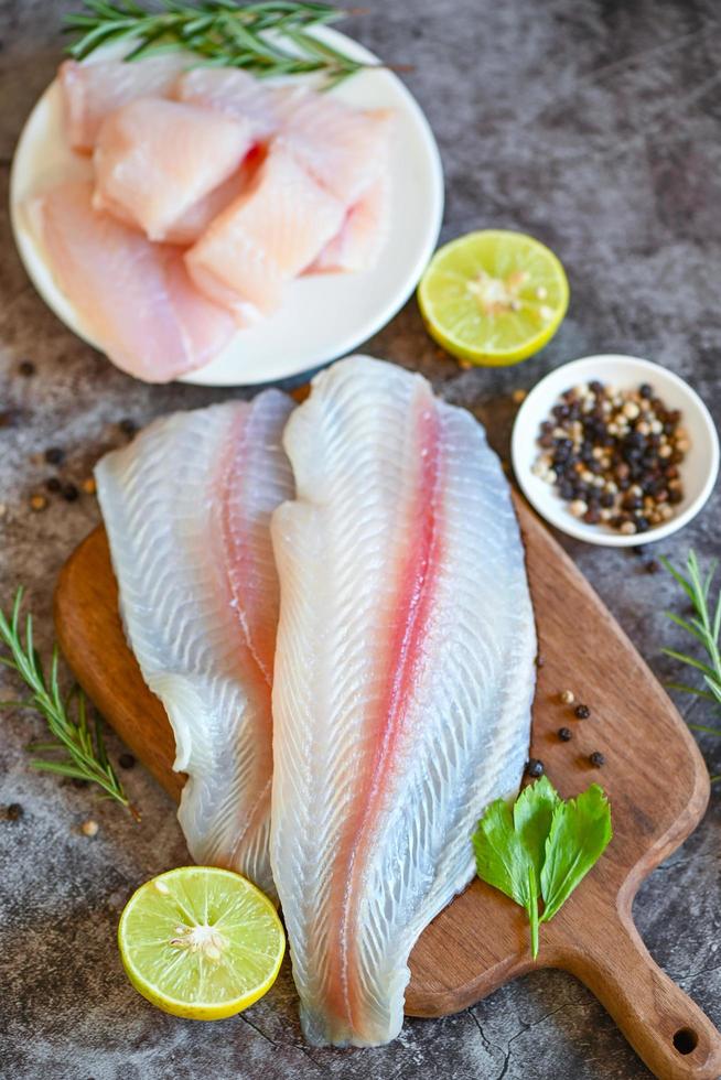 fish fillet on wooden board with ingredients for cooking, meat dolly fish tilapia striped catfish, fresh raw pangasius fish fillet with herb and spices black pepper lemon lime photo