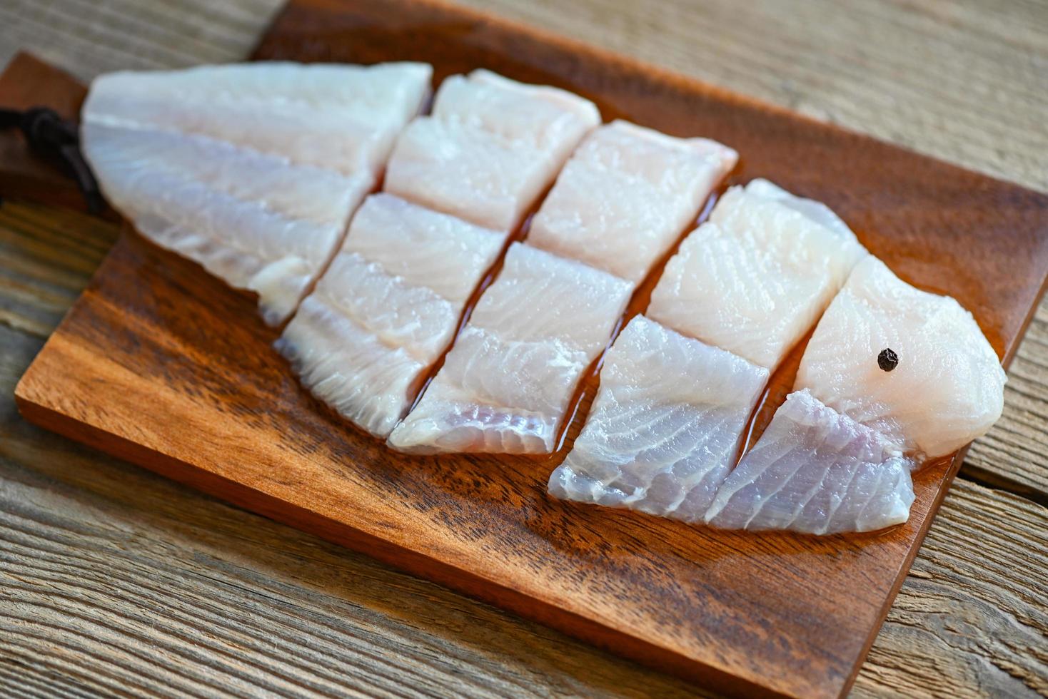 filete de pescado en una tabla de madera con ingredientes para cocinar, carnívoro de carne tilapia bagre rayado, filete de pescado pangasius crudo fresco foto