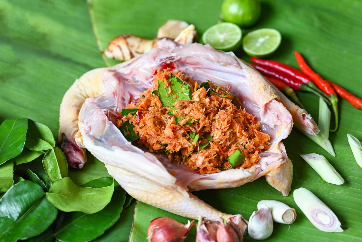 Thai food cooking with fresh chicken vegetables herbs and spices ingredients on banana leaf background, raw chicken with  lemon lime shallot garlic galangal lemon grass and chili photo