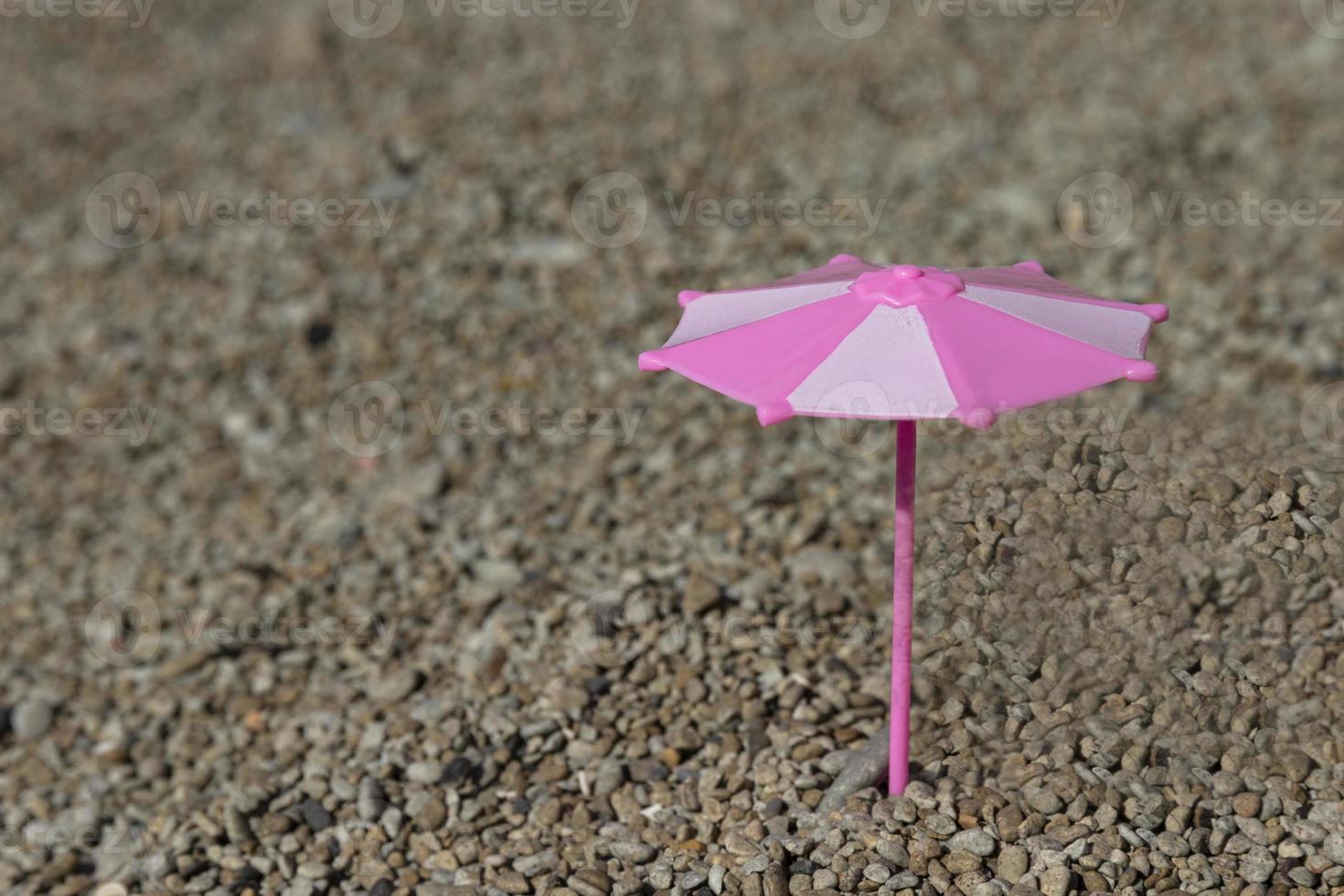 Toy umbrella in pink and white colors on the beach, by the sea. Selective focus. photo