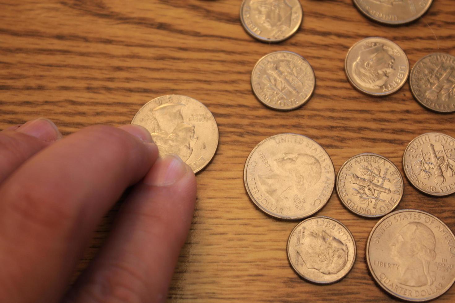 mano recogiendo un cuarto de moneda en moneda americana esparcida en el suelo de madera foto