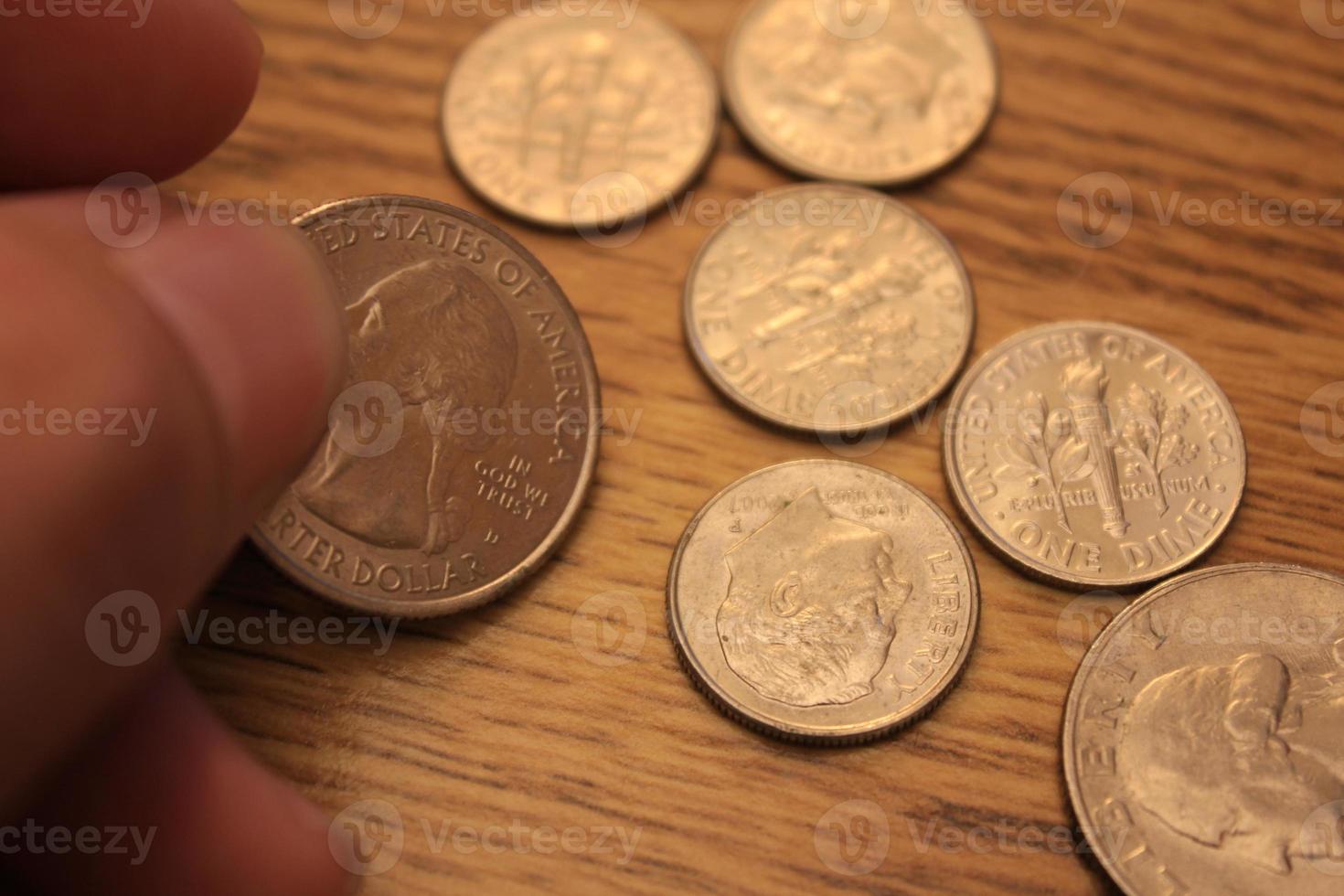 mano recogiendo un cuarto de moneda en moneda americana esparcida en el suelo de madera foto