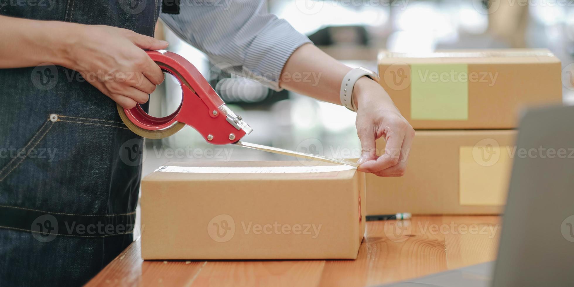 Small business entrepreneur SME, asian young woman,girl owner packing product, checking parcel for delivery to customer, using scotch tape to seal the box, working at home. Merchant online, e commerce photo