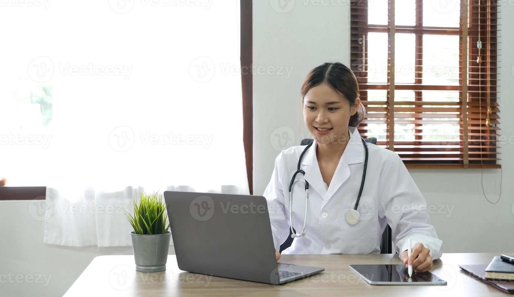 Portrait of young asian female doctor smiling and looking at camera sitting in examination room. photo