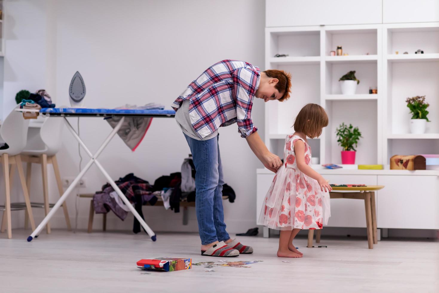 mother helping daughter while putting on a dress photo