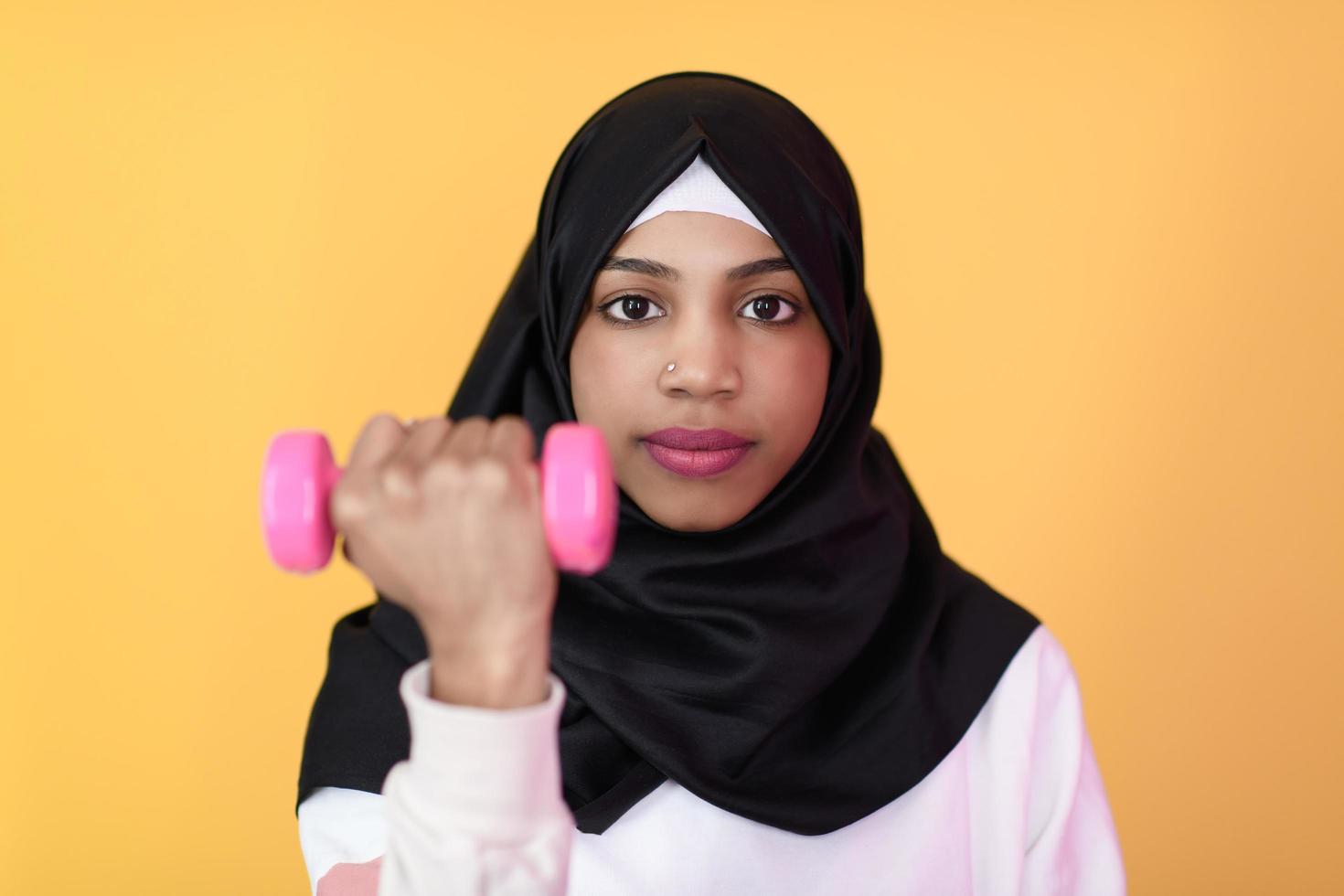 mujer musulmana afro promueve una vida saludable, sosteniendo pesas en sus manos foto