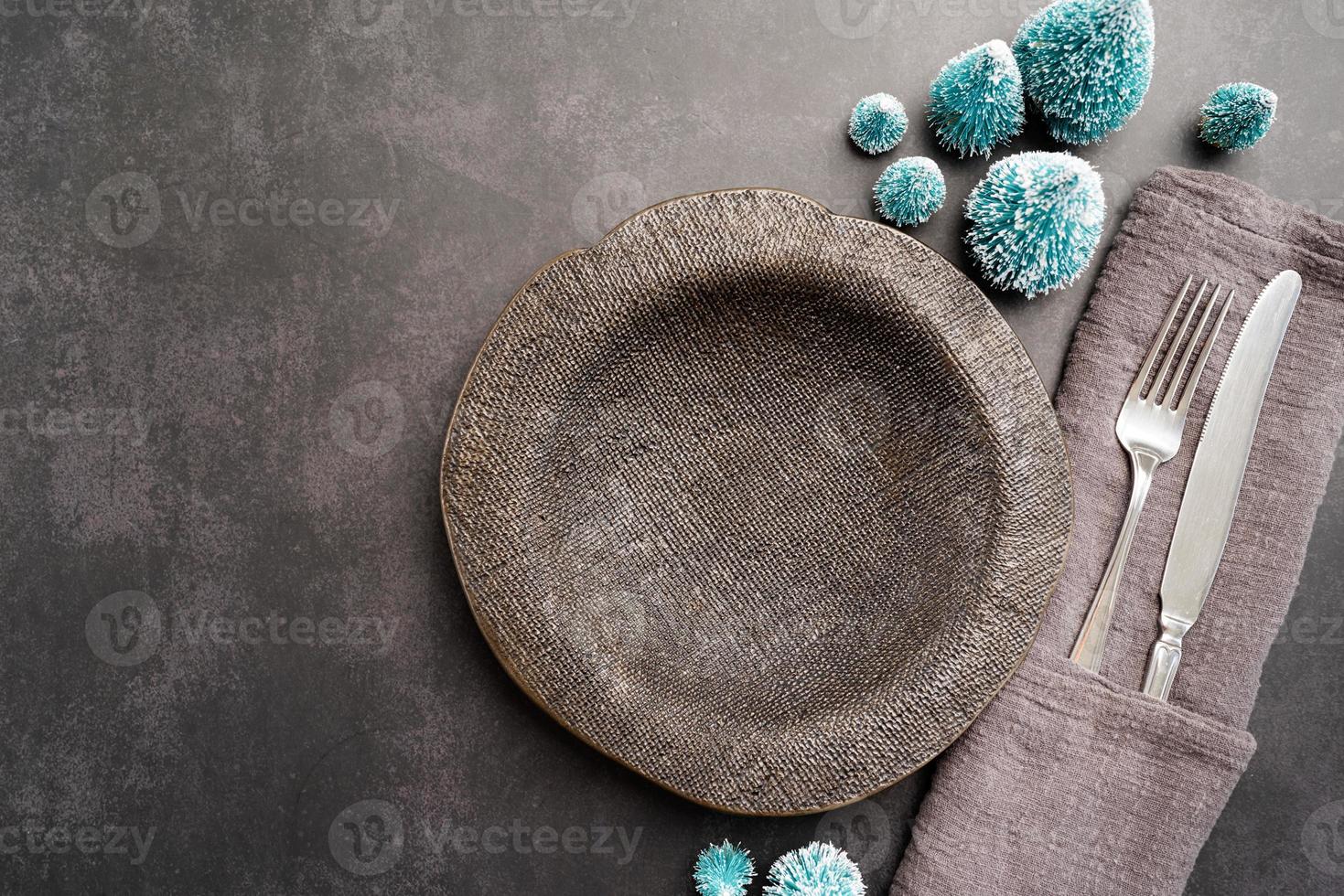 Christmas table setting with black dishware, silverware and green decorations on dark background. Top view. photo