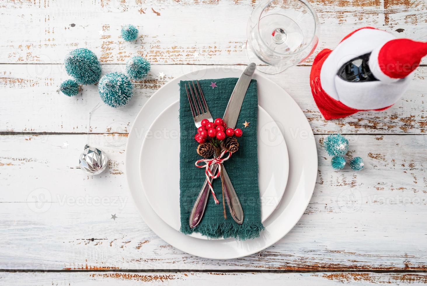 Christmas table setting with white dishware, silverware and red and green decorations on white wooden background. Top view. photo
