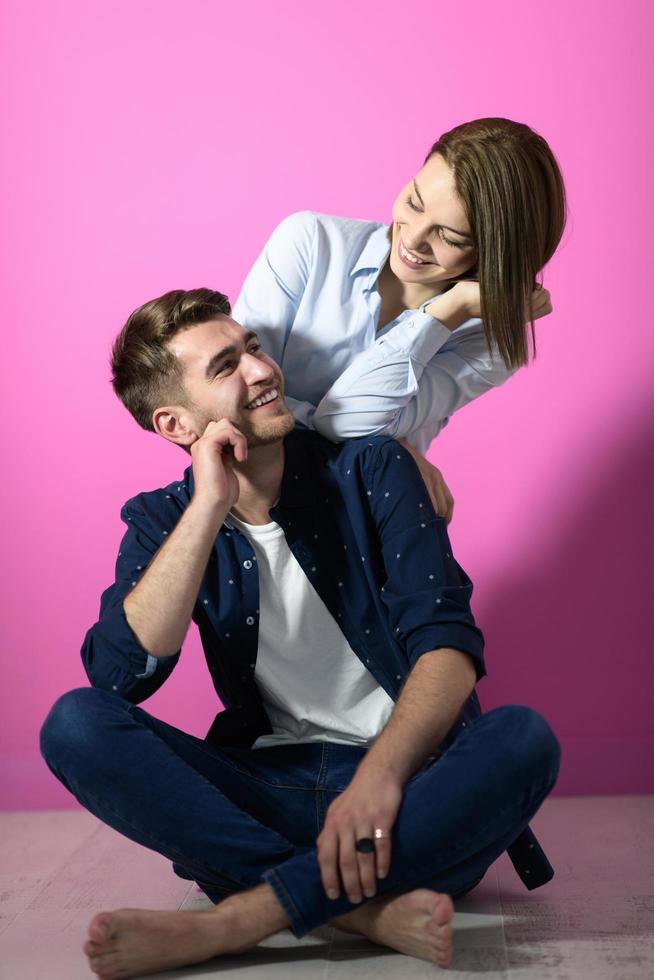 couple sitting on the floor while posing in front of a pink background photo