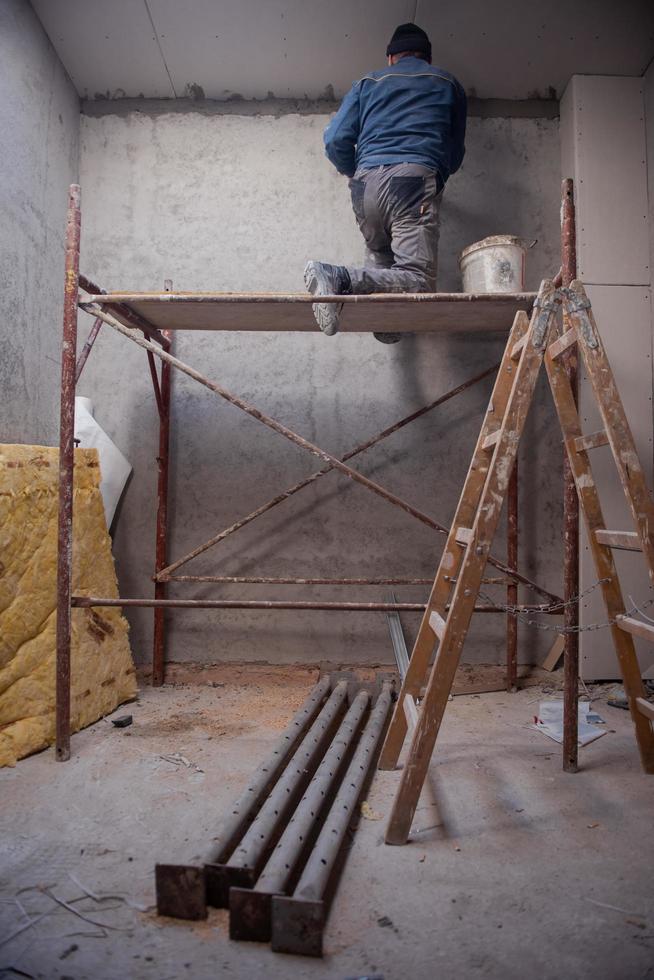 trabajador de la construcción enyesado en el techo de yeso foto