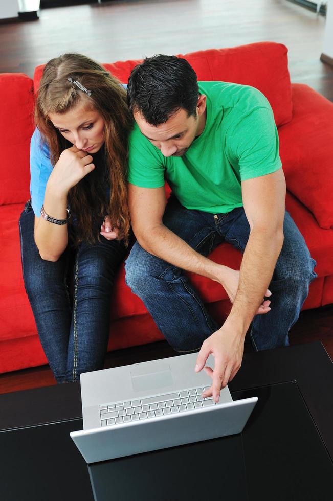 happy couple have fun and work on laptop at home on red sofa photo