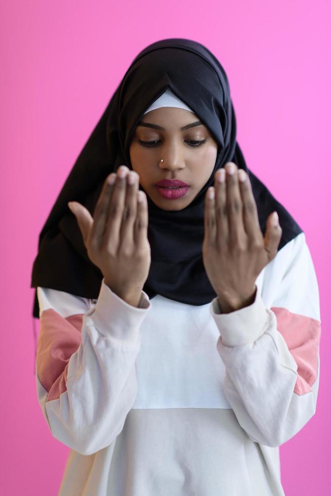 mujer musulmana africana moderna hace oración tradicional a dios, mantiene las manos en gesto de oración, usa ropa blanca tradicional foto