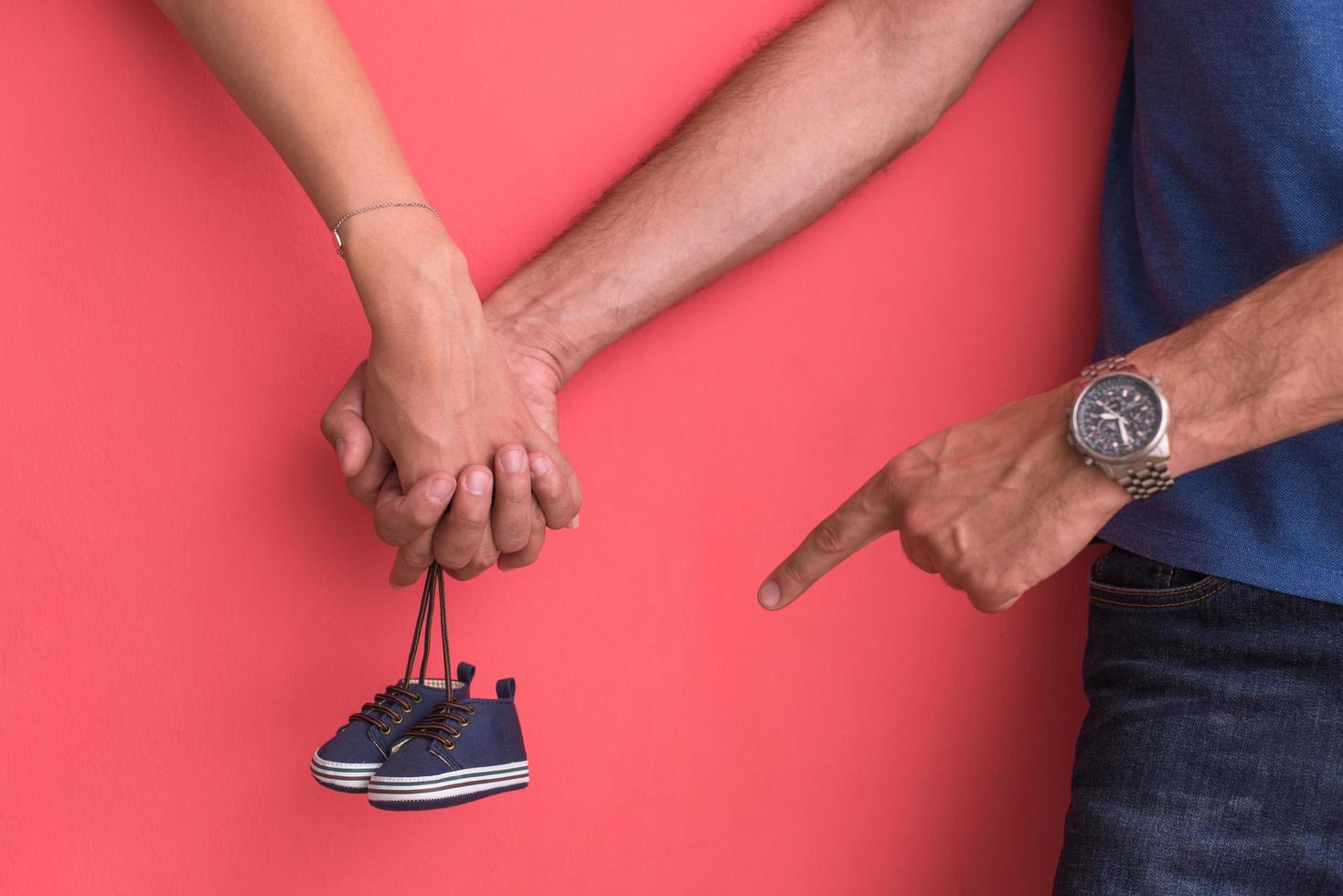 young pregnant couple holding newborn baby shoes photo