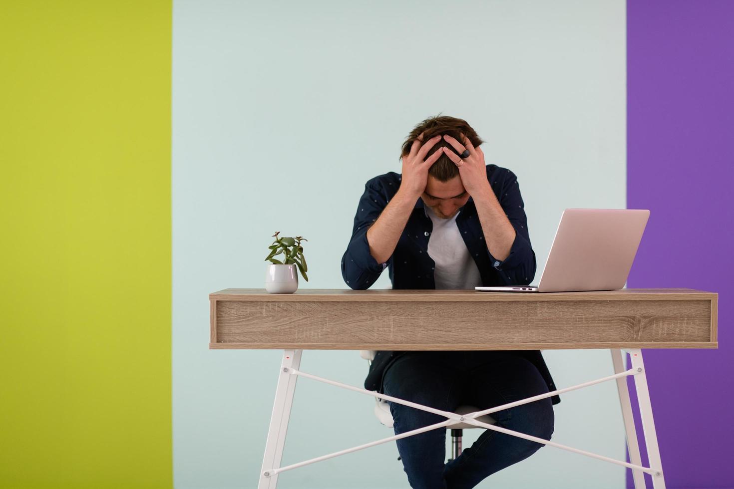 disappointed and annoyed man sitting at a table and looking at a laptop photo