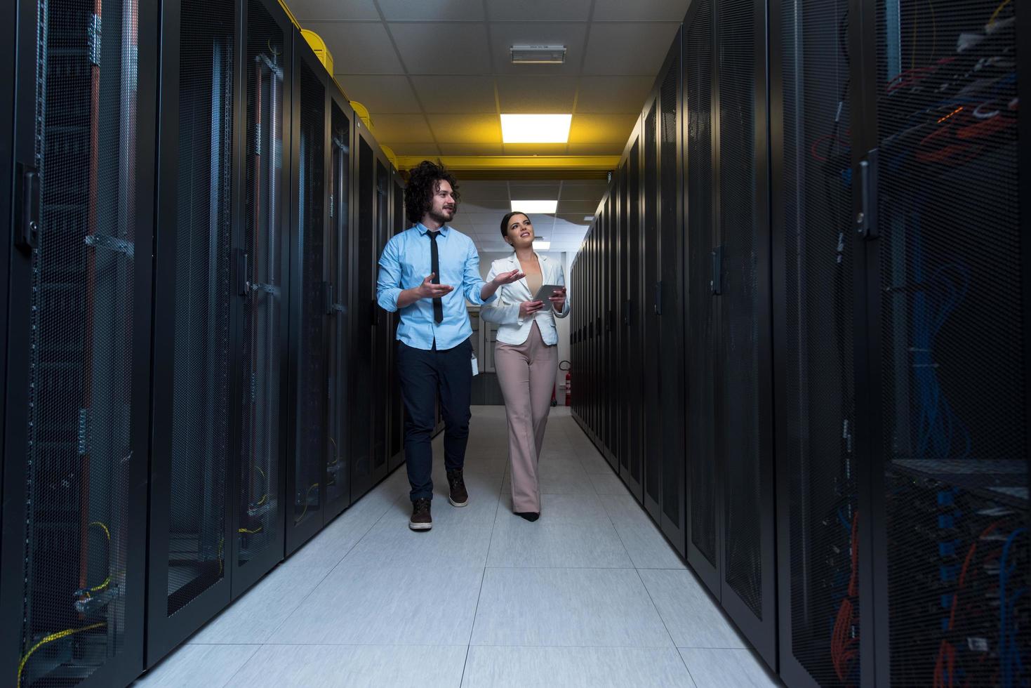 engineer showing working data center server room to female chief photo