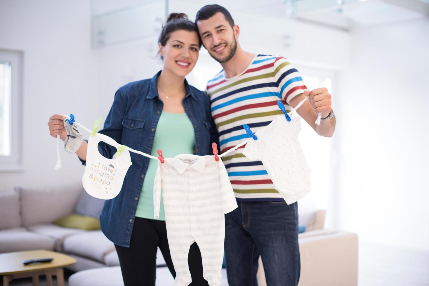 young couple holding baby bodysuits at home photo