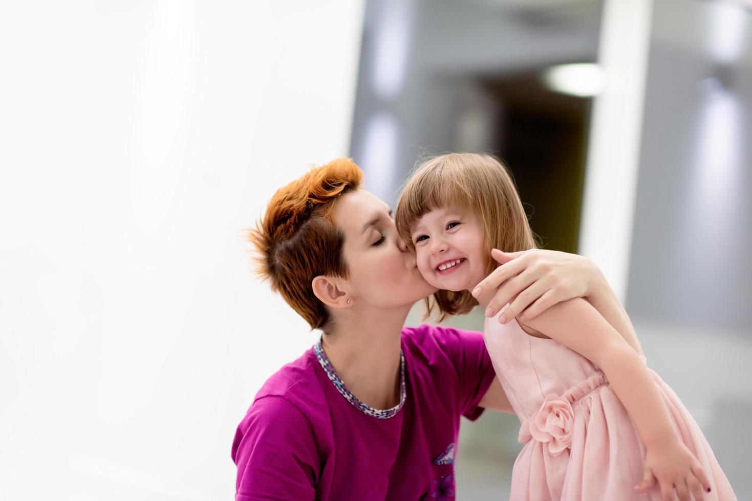 young mother helping daughter while putting on a dress photo