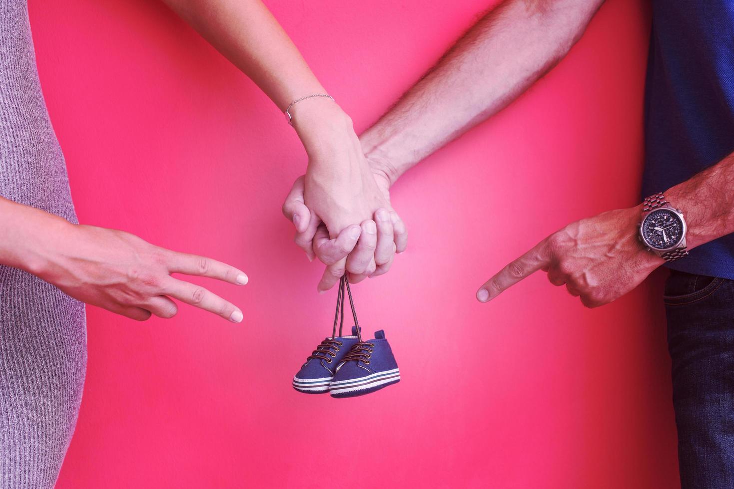 young pregnant couple holding newborn baby shoes photo