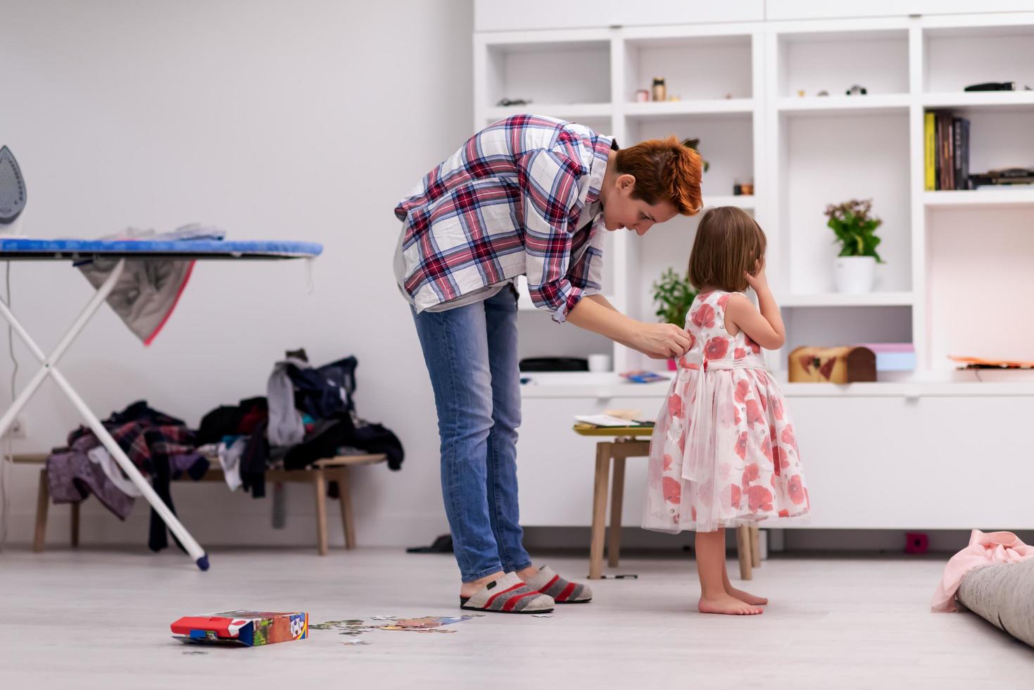 mother helping daughter while putting on a dress photo