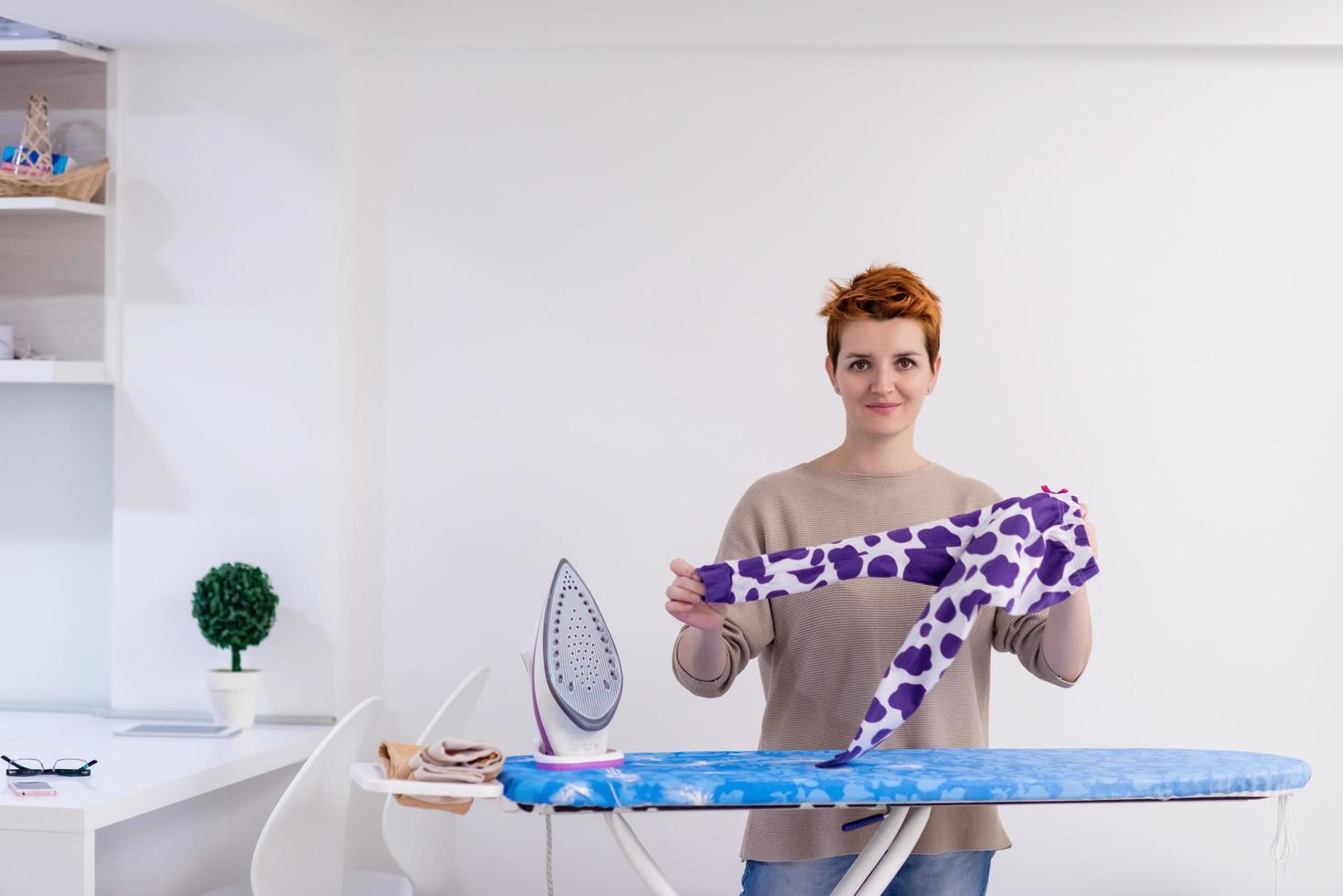 mujer pelirroja planchando ropa en casa foto