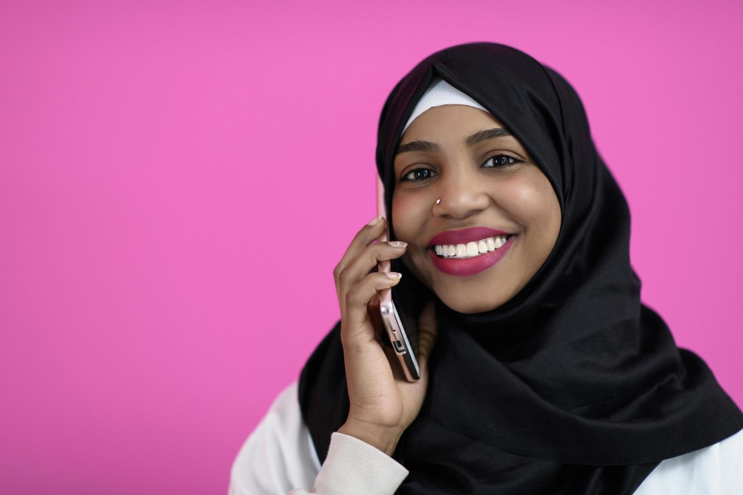 mujer afro usa un teléfono celular frente a un fondo rosa foto