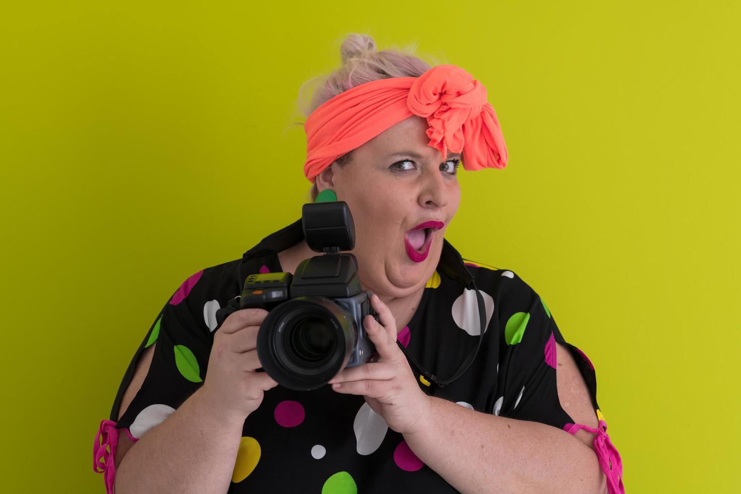 plus size smiling woman with funny emotional face expression with vintage camera in dress isolated on green background, traveler on vacation, summer fashion style, excited tourist. photo